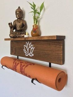 a buddha statue sitting on top of a wooden shelf next to a yoga mat and potted plant