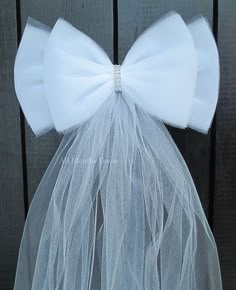 a white veil with a large bow on the top is hanging from a wooden fence