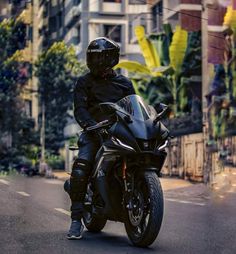 a man riding on the back of a black motorcycle down a street next to tall buildings