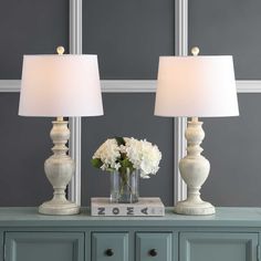 two white lamps sitting on top of a table next to a vase filled with flowers