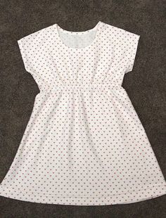 a white dress with red polka dots on the front and bottom, sitting on a carpeted floor