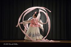 a woman in a white dress is spinning a pink ribbon