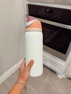 a person holding up a white and orange insulated water bottle in front of an oven