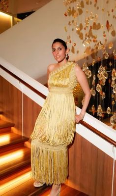 a woman in a yellow dress standing next to a stair case and chandelier