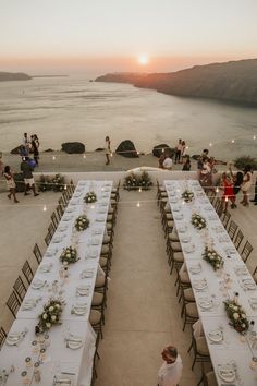 an outdoor dining area overlooking the ocean with long tables and chairs set up for dinner