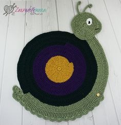 a crocheted round rug with a green and purple snail on the center, sitting on a white wooden floor