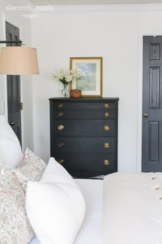 a bedroom with black dresser and white bedding