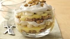 a dessert with bananas, whipped cream and nuts in a glass bowl on a table