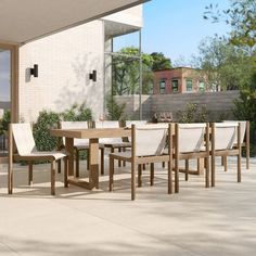 an outdoor dining table and chairs with white cushions on the outside patio, next to a brick building