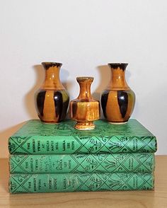 three vases are sitting on top of two books, one is green and the other is gold