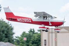 a small red and white plane flying low to the ground with it's landing gear down