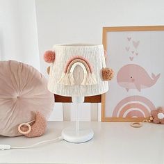 a pink lamp shade with pom poms sits on a table next to other items