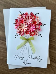 a birthday card with pink flowers and green ribbon on it, sitting on a wooden table