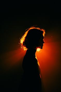 the silhouette of a woman's head against a dark background with light coming from behind her