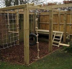 an outdoor play area with climbing ropes and a swing set in the back yard, next to a wooden fence