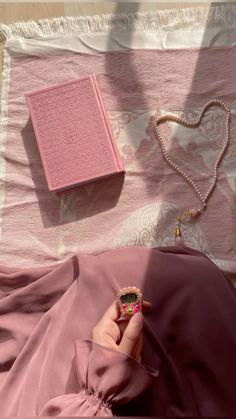 a person is laying on a bed with a pink blanket and some jewelry next to them