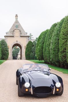 a black sports car parked in front of a stone building with an archway and trees behind it