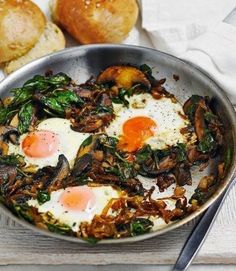 two fried eggs and spinach in a pan next to rolls on a white towel