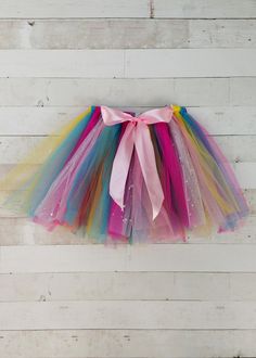 a multicolored tulle skirt hanging on a white wooden wall with a pink bow