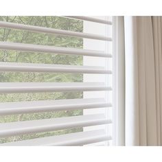 a window with white blinds and trees in the background