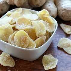 a white bowl filled with sliced up bananas next to some ginger chips on a wooden table