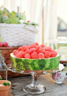 a watermelon covered cake sitting on top of a wooden table next to potted plants