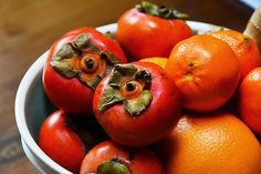 a bowl filled with oranges and tomatoes on top of a wooden table next to a banana