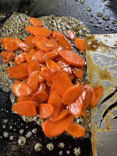 carrots being cooked in oil and water on a stove top with a spatula