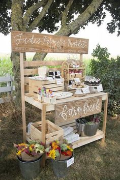 a wooden stand that has some food on it and flowers in buckets next to it