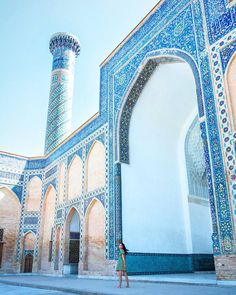 a woman standing in front of a building with blue and white tiles on the walls