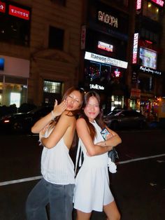 two young women standing next to each other in front of a tall building at night