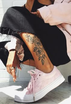 a woman sitting on the ground with her legs crossed and flowers tattooed on her leg