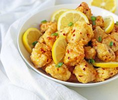 a white bowl filled with fried chicken and lemon wedges on top of a table