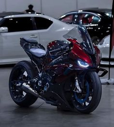 a red motorcycle parked next to two white cars in a showroom with other vehicles