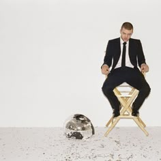 a man in a suit sitting on a chair next to a soccer ball and looking at the camera