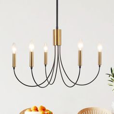 a chandelier hanging over a dining room table with fruit on it and candles