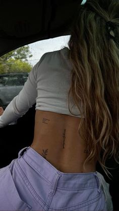 a woman sitting in the back seat of a car with tattoos on her lower back