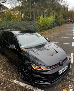 a black car parked in a parking lot next to a fallen down tree on the ground