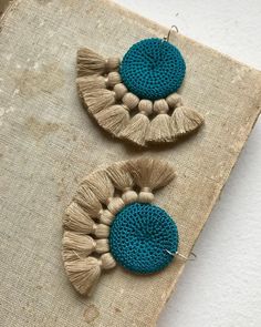 two earrings with tassels are sitting on a piece of fabric