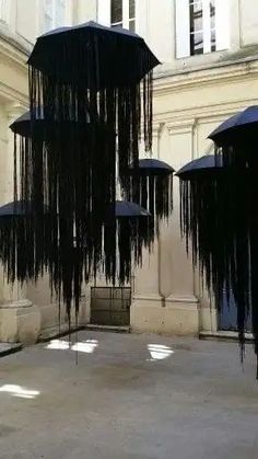 several black umbrellas hanging from the ceiling in an empty courtyard with shadows on the ground