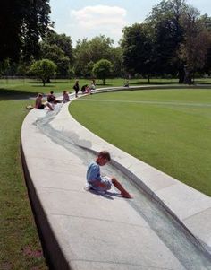 a boy sitting on the edge of a concrete wall in a park with other people