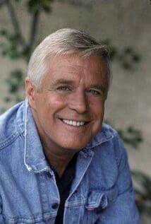 an older man wearing a denim shirt and smiling at the camera with his hands in his pockets