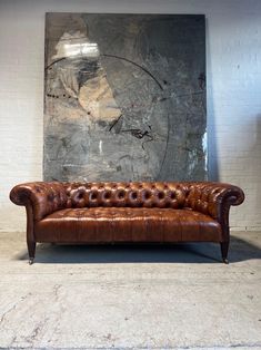 a brown leather couch sitting in front of a wall with a painting on it's side