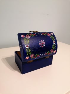 a blue box with flowers painted on it sitting on top of a white table next to a wall