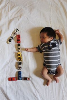 a baby laying on top of a white sheet next to toy cars and letters that spell out the word i