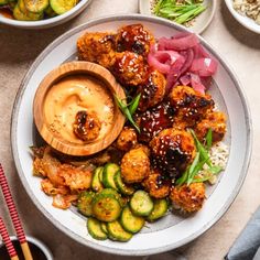 a white plate topped with meat and veggies next to bowls of dipping sauce