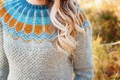 a woman with long blonde hair wearing a blue and orange sweater in the grass,