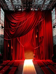 an empty stage with red drapes and benches on the floor, in front of a bright light