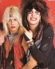 two women with long hair and piercings posing for a photo in front of a red wall