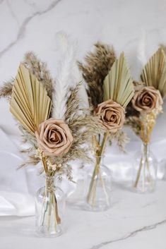 three vases with dried flowers in them on a marble countertop, one is filled with feathers and the other two are empty